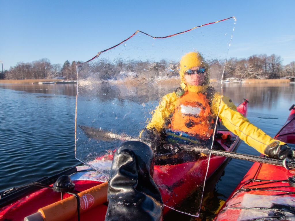 A kayaker framed through a transparent ice sheet held up close