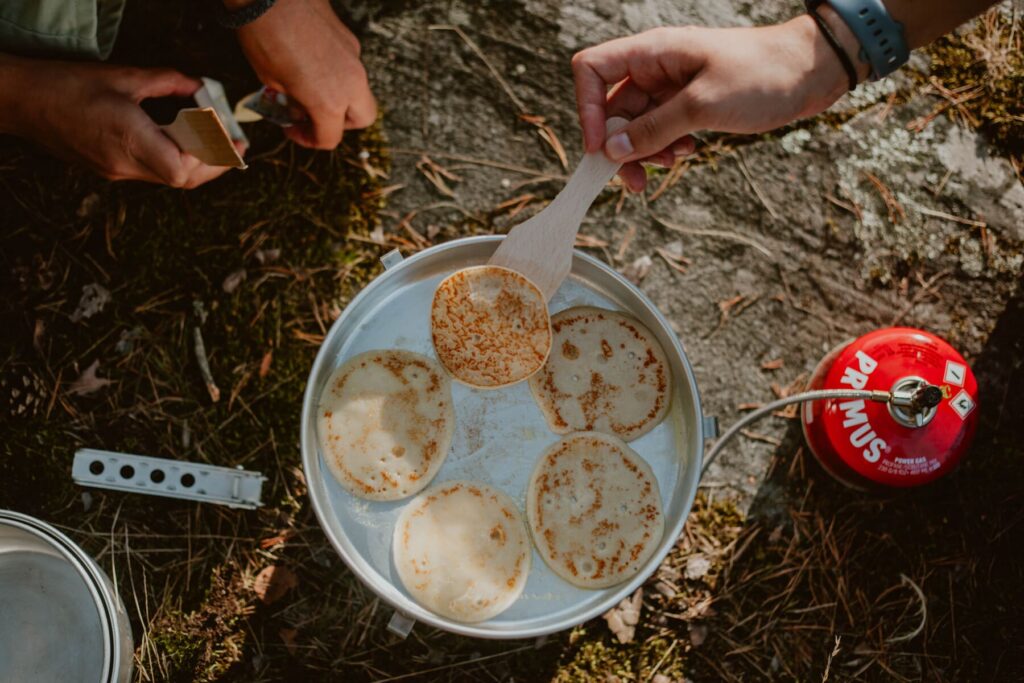 Pancakes frying on a Trangia stove outdoors during a camping trip.