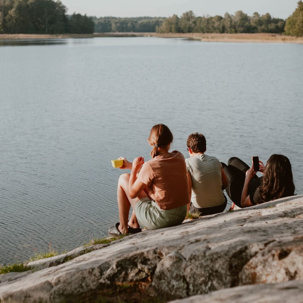 Three girls sitting on a rock by the water, relaxing and enjoying the moment in Bogesund Nature Reserve.