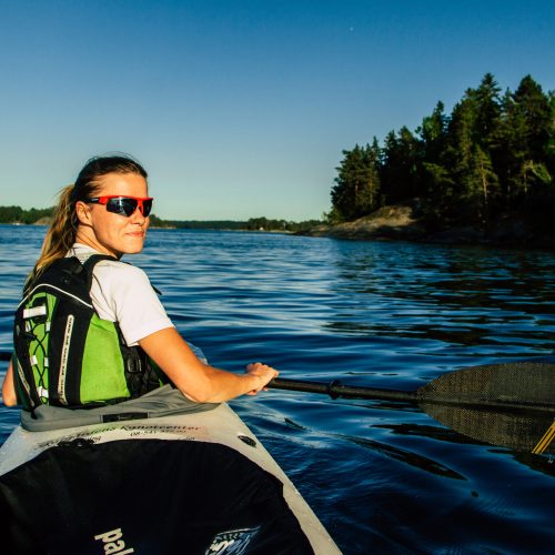 Smiling woman paddling in a tandem expedition kayak, with beautiful islands in the background.