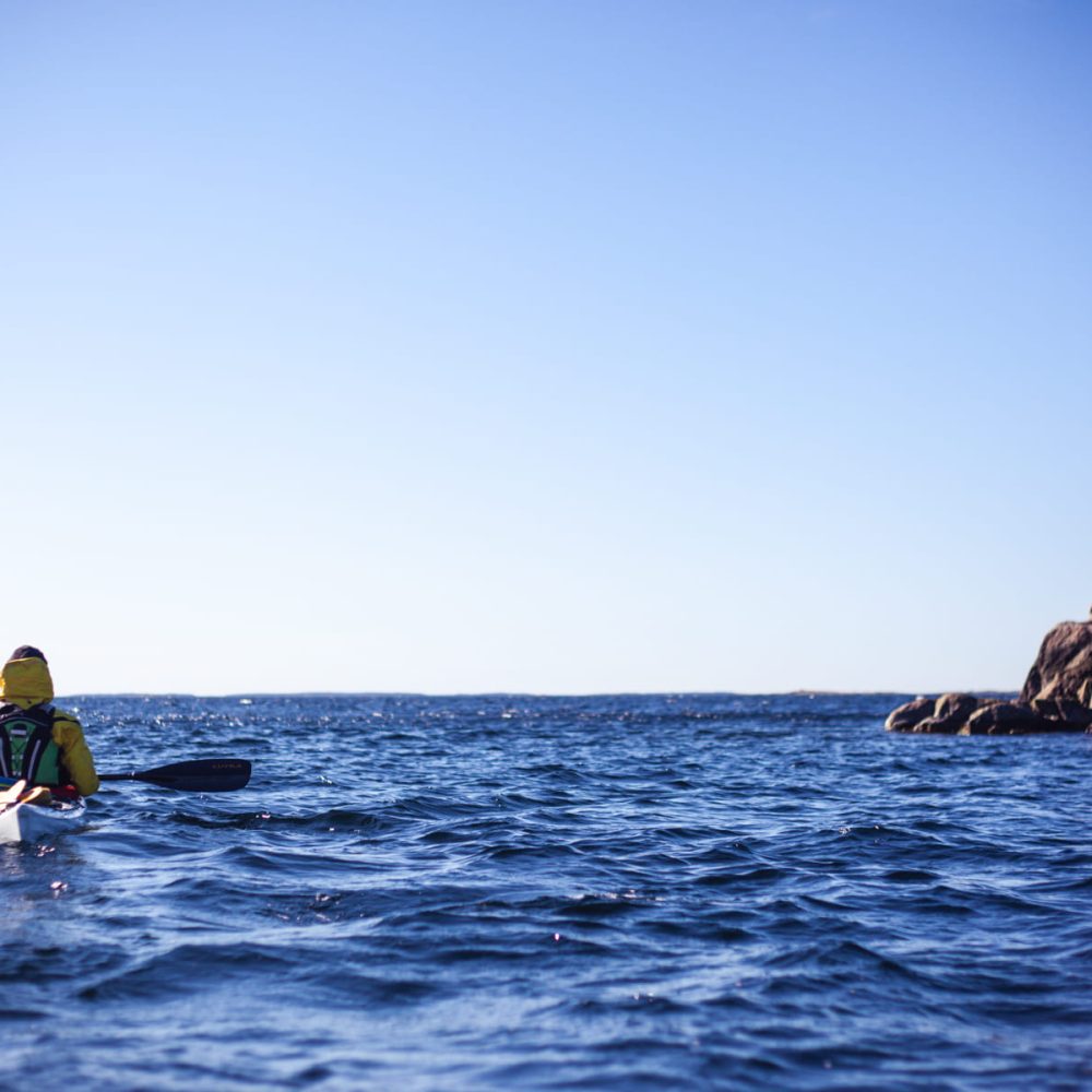 Transitioning from rocky shores to open waters, a kayaker ventures toward the horizon